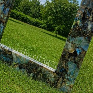 Puede incluir: Espejo cuadrado con marco de mosaico de piedras azules, verdes y negras. El espejo refleja un c&eacute;sped verde y &aacute;rboles. El texto "stoneviaheritage" es visible en el marco.