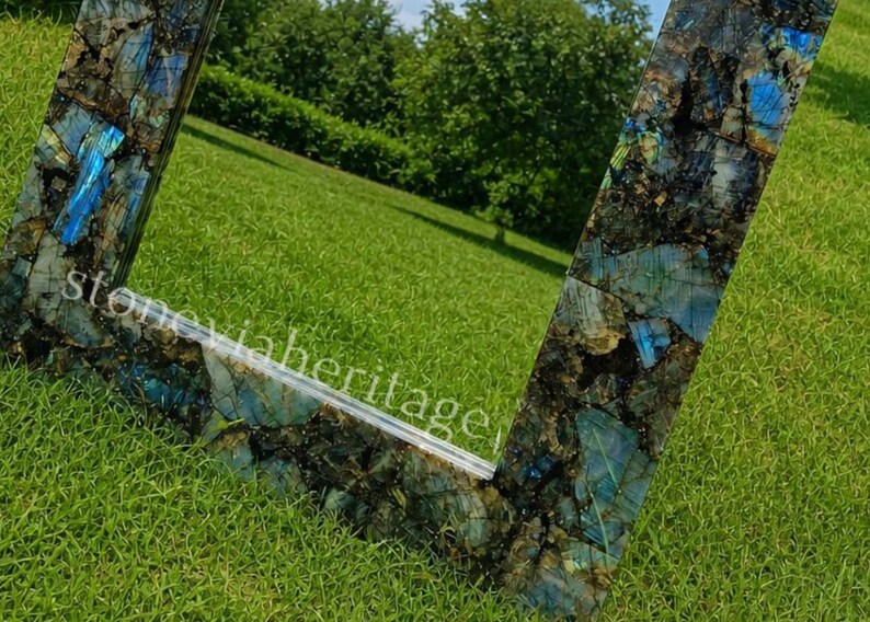 Puede incluir: Espejo cuadrado con marco de mosaico de piedras azules, verdes y negras. El espejo refleja un c&eacute;sped verde y &aacute;rboles. El texto "stoneviaheritage" es visible en el marco.