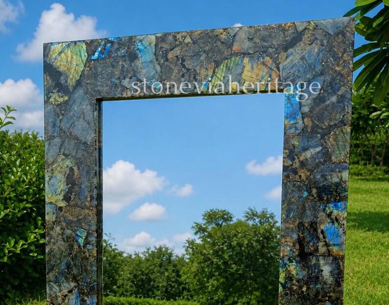 Puede incluir: Espejo rectangular con marco de mosaico de piedras azules, verdes y marrones. El texto "stoneviaheritage" es visible en la parte superior del marco. El espejo refleja un cielo azul con nubes blancas y &aacute;rboles verdes.