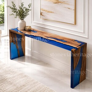 Pode incluir: Uma mesa de consola moderna com um tampo de madeira de borda viva e incrustações de resina azul. A mesa tem uma forma retangular com grão de madeira natural e detalhes em resina azul. As pernas também são feitas de madeira e resina azul.