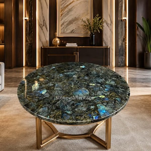 May include: A round coffee table featuring a polished labradorite stone top with deep blue, green, and black crystalline patterns. The table is supported by a gold-toned metal base with a geometric frame. The text stoneviaheritage is visible.