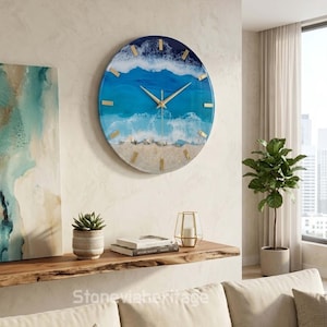 May include: A round wall clock featuring a resin art design of ocean waves crashing onto a sandy beach. The clock face displays shades of deep blue, turquoise, and white foam, accented with gold-colored hour markers and thin gold-colored hands.