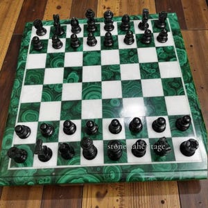 Op de afbeelding: Een schaakspel met een schaakbord van malachiet en marmer en zwarte schaakstukken. Het bord heeft een groene malachietrand en afwisselend witte en groene vierkanten. De schaakstukken zijn zwart en op het bord geplaatst.