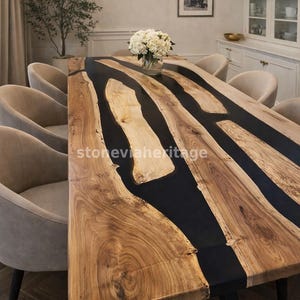 Puede incluir: Una mesa de comedor rectangular grande con una superficie de vetas de madera natural e incrustaciones de resina epoxi negra. La mesa está rodeada de sillas tapizadas beige. Las dimensiones de la mesa no son visibles en la imagen.