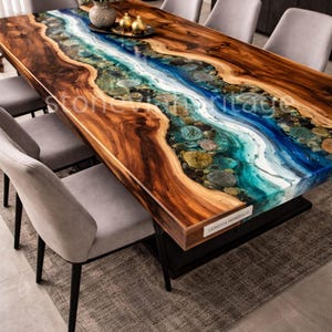 Op de afbeelding: Een grote, rechthoekige houten eettafel met een rivierachtig epoxyharsontwerp in tinten blauw, wit en teal. De tafel is omringd door grijze gestoffeerde stoelen. Het houten oppervlak van de tafel heeft een natuurlijk nerfpatroon.