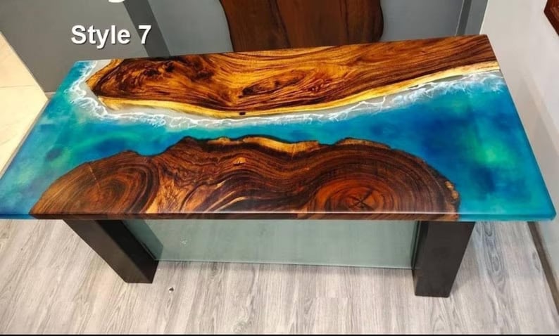 May include: Rectangular wooden table with a unique design. The tabletop features a combination of natural wood and a blue resin that resembles the ocean. The table has dark brown legs and the text "Style 7" in the top left corner.