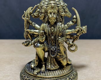 Könnte beinhalten: Eine metallisch goldfarbene Figur einer Gottheit mit fünf Köpfen und zehn Armen, die auf einem runden Sockel kniet. Die Figur trägt verzierten Schmuck und hält verschiedene symbolische Gegenstände in den Händen, mit detaillierten Verzierungen.