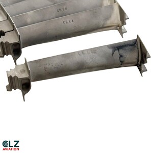 May include: Two metallic turbine blades with a matte gray finish. The top blade features the stamped text CR 50 and CR KE. The bottom blade has a smooth, elongated shape with a dark, weathered patch on the right side and a complex root structure.