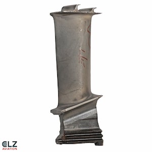 May include: A silver-colored turbine blade with a curved design and two prongs at the top. The blade has a rectangular base with horizontal grooves and a diagonal cut. Red markings are visible on the blade's surface. The logo "OLZ AVIATION" is at the bottom.