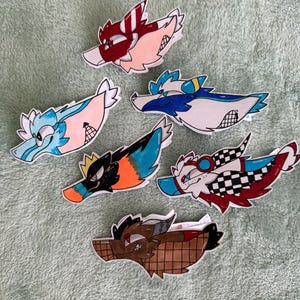 May include: Six illustrated paper dragon puppets with the text Mini cedar point dragon puppets! The designs feature various color schemes including red and white stripes, blue and white, black and orange, and a brown grid pattern with red accents.