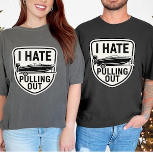 May include: Two t-shirts, one grey and one black, each with a graphic that reads "I HATE PULLING OUT" above a boat illustration. The design is in a white shield shape.