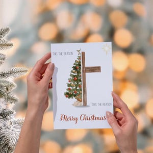 Könnte beinhalten: Eine Weihnachtskarte mit einem Aquarelldesign. Die Karte zeigt einen Weihnachtsbaum und ein Kreuz. Der Text auf der Karte lautet "This the season, This the reason, Merry Christmas."