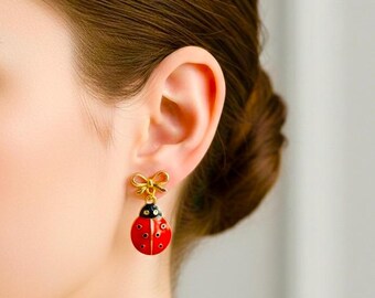 May include: Gold-toned ladybug earrings with red enamel bodies and black spots. Each earring features a gold bow detail at the top. The earrings are a whimsical accessory.