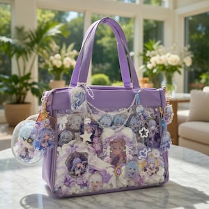 May include: A lilac tote bag with a clear front panel filled with character-themed accessories. The bag has matching handles and is adorned with charms, keychains, and decorative elements in shades of purple, white, and blue. The bag is sitting on a marble table.