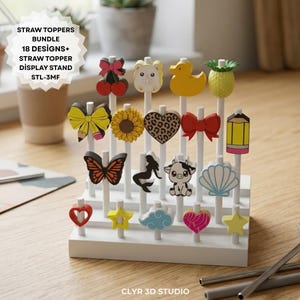 Op de afbeelding: Een witte displaystandaard met 18 kleurrijke strotoppers met diverse ontwerpen, waaronder een kers, beer, eend, ananas, strik, zonnebloem, hart, vlinder, zeemeermin, koe en schelp. De tekst op de afbeelding luidt "STRAW TOPPERS BUNDLE 18 DESIGNS+ STRAW TOPPER DISPLAY STAND STL-3MF".