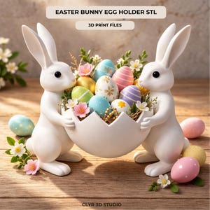 Op de afbeelding: Twee witte konijnenbeeldjes die een witte eivormige mand vasthouden gevuld met kleurrijke paaseieren en bloemen. De eieren zijn versierd met verschillende patronen en kleuren. De tekst "EASTER BUNNY EGG HOLDER STL" en "3D PRINT FILES" zijn zichtbaar.