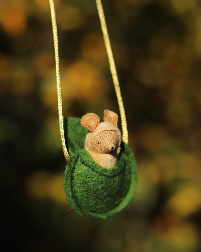 May include: A small, brown, plush mouse is sitting in a green felt pouch hanging from a yellow cord. The pouch is shaped like a leaf and has a drawstring closure.