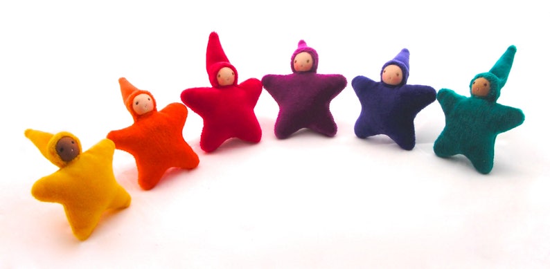 May include: Six felt star-shaped dolls with wooden faces and pointed hats. The dolls are arranged in a rainbow pattern, starting with yellow and ending with green.