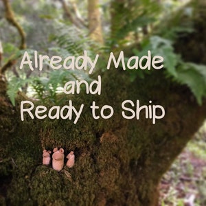 May include: A close-up of a mossy tree trunk with the text "Already Made and Ready to Ship" written on it. Four small, brown, ceramic figures are sitting on the trunk.