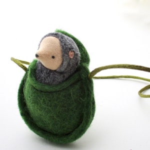 May include: A small gray and white stuffed hedgehog is nestled inside a green felt pouch with a green cord.