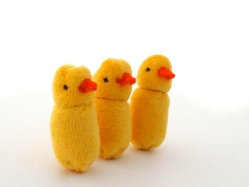Op de afbeelding: Drie handgemaakte gele kuikenfiguren met oranje snavels en zwarte ogen. De kuikens zijn gemaakt van een zacht, getextureerd materiaal, mogelijk stof of garen. Ze staan rechtop tegen een witte achtergrond.