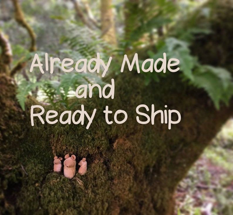 Pode incluir: A imagem mostra tr&ecirc;s pequenas figuras de ratos de madeira de cor clara, aninhadas num tronco de &aacute;rvore coberto de musgo. O texto "Already Made and Ready to Ship" est&aacute; sobreposto na imagem. O fundo &eacute; uma vista desfocada de uma floresta.