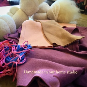 Pode incluir: Uma cole&ccedil;&atilde;o de materiais de artesanato, incluindo tecido rosa, bege e roxo, formas brancas recheadas e fio azul e rosa. O texto "Handmade in our home studio" &eacute; vis&iacute;vel na parte inferior da imagem.