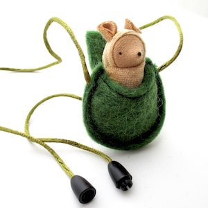 May include: A green felt pouch with a drawstring closure, containing a small stuffed animal with a beige body and a brown nose. The pouch is attached to a green cord with black cord ends.