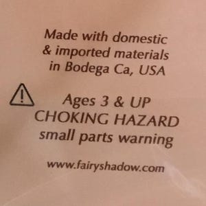 May include: Text on a white background reads "Made with domestic & imported materials in Bodega Ca, USA." Below is a warning symbol and text: "Ages 3 & UP CHOKING HAZARD small parts warning." The website www.fairyshadow.com is also displayed.