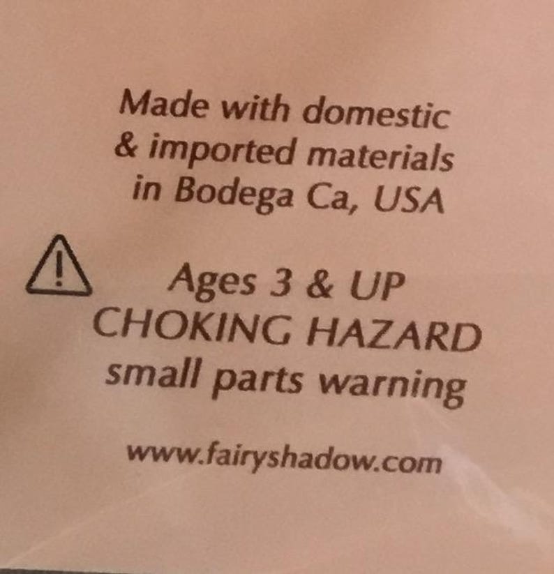 May include: Text on a white background reads "Made with domestic & imported materials in Bodega Ca, USA." Below is a warning symbol and text: "Ages 3 & UP CHOKING HAZARD small parts warning." The website www.fairyshadow.com is also displayed.