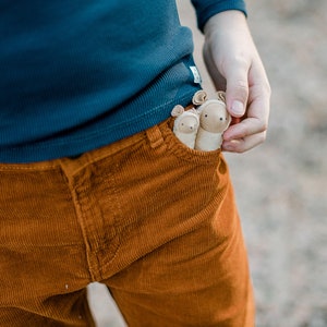 May include: Two small, brown, plush animal toys with ears sticking out of a brown corduroy pocket.