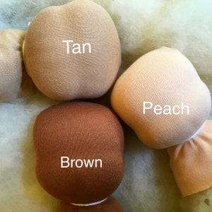 Pode incluir: Close-up de cabe&ccedil;as de bonecas nas cores castanho, p&ecirc;ssego e bege. A palavra "Tan" est&aacute; impressa na cabe&ccedil;a bege, "Peach" na cabe&ccedil;a p&ecirc;ssego e "Brown" na cabe&ccedil;a castanha. As cabe&ccedil;as das bonecas s&atilde;o feitas de tecido macio.