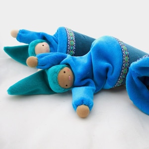 May include: Two blue fabric dolls with embroidered faces and blue and green patterned fabric. The dolls are lying on a white surface.