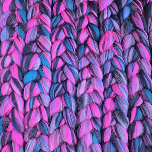 May include: Close-up of a chunky knit textile in a repeating braided pattern. The yarn is a blend of vibrant colours, including shades of pink, blue, and black. The texture appears soft and plush, suggesting a cosy blanket or throw.