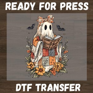 May include: A DTF transfer featuring a ghost wearing a floral bow and a patchwork quilt, reading an open book. The ghost is surrounded by autumn flowers, leaves, and two bats. The text READY FOR PRESS and DTF TRANSFER appears at the top and bottom.
