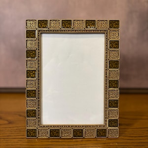 May include: A rectangular picture frame featuring a metallic gold border with an alternating pattern of dark olive green mosaic tiles and intricate gold filigree squares. The frame surrounds a blank white rectangular center display area.