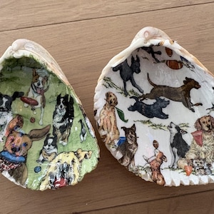 May include: Two decorative clam shells featuring decoupage illustrations of various dog breeds. The left shell has a green background with dogs playing with balls and frisbees. The right shell has a white background with dogs running and playing.