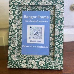 May include: A rectangular picture frame with a green floral pattern. The frame holds a blue card with the text "Bangor Frame" and a QR code. The text "Follow us on Instagram!" is also visible.