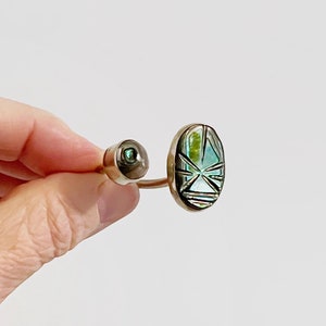 May include: A silver ring featuring a green abalone shell inlay. The ring is open and has a curved design.