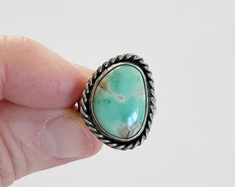 Puede incluir: Un anillo de plata con una piedra turquesa verde engastada en un diseño de cuerda.