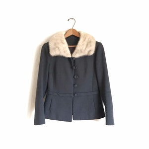 May include: A dark gray blazer with a white fur collar. The blazer has a button closure and a belt at the waist.