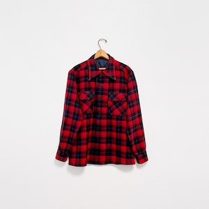 May include: A red and black plaid button-down shirt with long sleeves, hanging on a wooden hanger. The shirt has two chest pockets and a navy blue lining at the collar. The classic lumberjack style is visible.