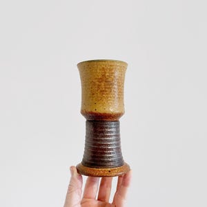 May include: A brown and tan ceramic goblet with a flared top and a textured base.
