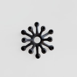 May include: A black, starburst-shaped candle holder with 12 individual candle holders arranged around a central hole. The candle holder is made of a dark, possibly metal material, and sits against a white background.