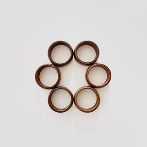 May include: Set of six brown wooden napkin rings arranged in a circle on a white background.