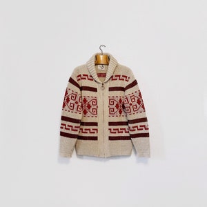 May include: A cream-colored cardigan with a zipper closure and a red and cream geometric pattern. The cardigan has a collar and long sleeves.