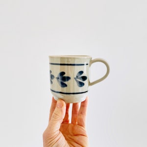May include: A white ceramic mug with a blue floral design. The mug has a handle and is slightly wider at the top than the bottom.