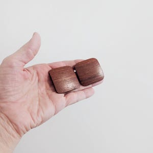 May include: Two square-shaped wooden pieces with rounded corners and a smooth, polished finish. The wood displays a rich, dark brown grain pattern with visible natural textures, presented as a pair of matching flat, solid components.