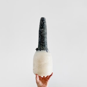 May include: A tall, white ceramic vase with a dark blue and green glaze on the top half. The vase has a narrow neck and a wide base.