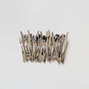 May include: An assortment of polished stainless steel cutlery, comprising forks, knives, and spoons, set against a white backdrop. The utensils are arranged in a neat manner, reflecting the ambient light.